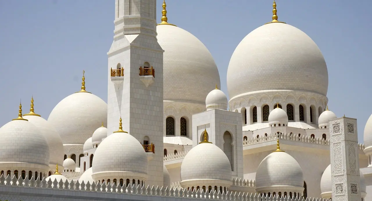 White marble domes and reflective pools of Sheikh Zayed Grand Mosque during sunset